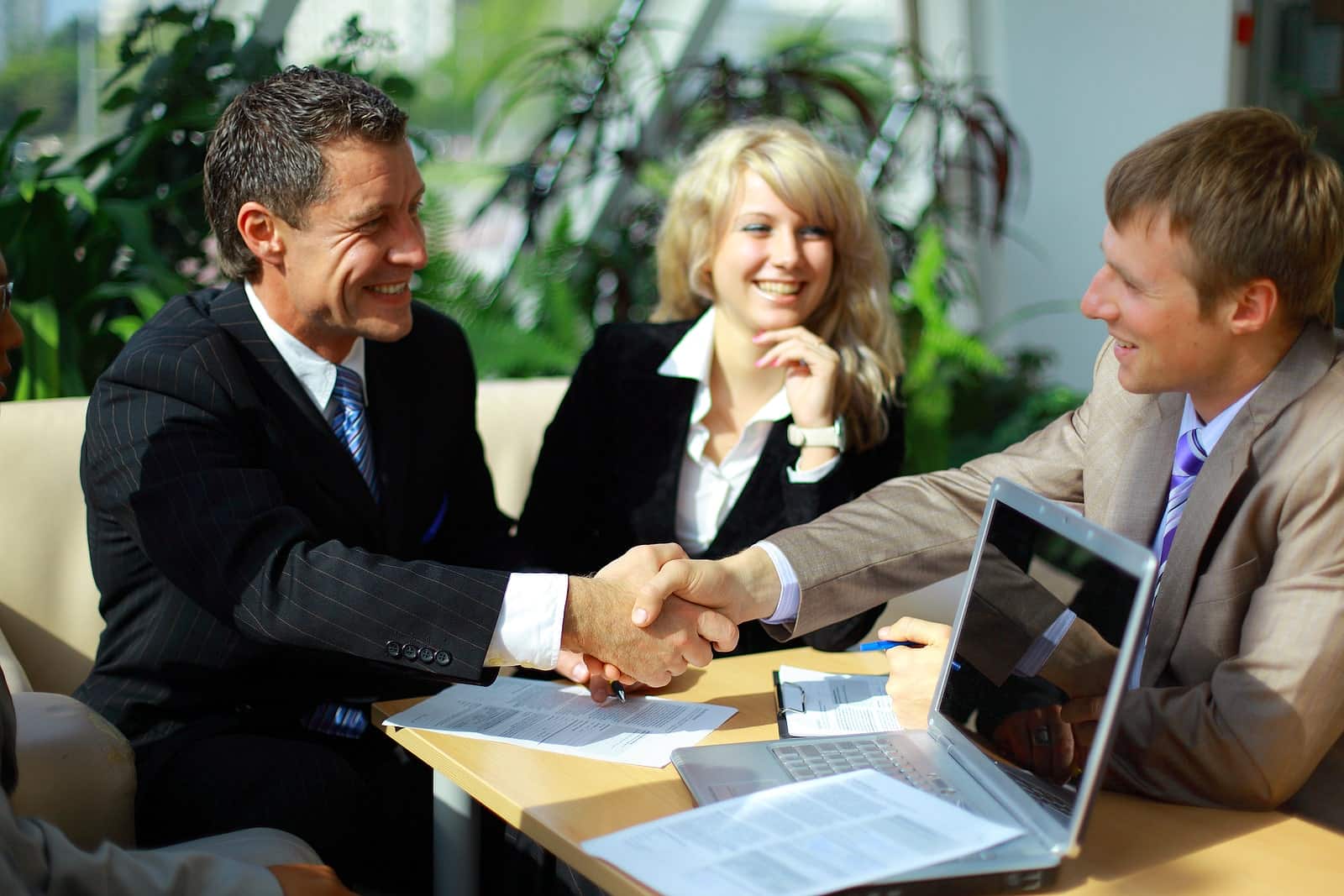 A group of business people shaking hands and smiling at a desk.