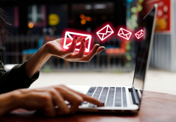 Image of a person typing on a laptop with one hand while envelope graphics move from their other hand into the computer