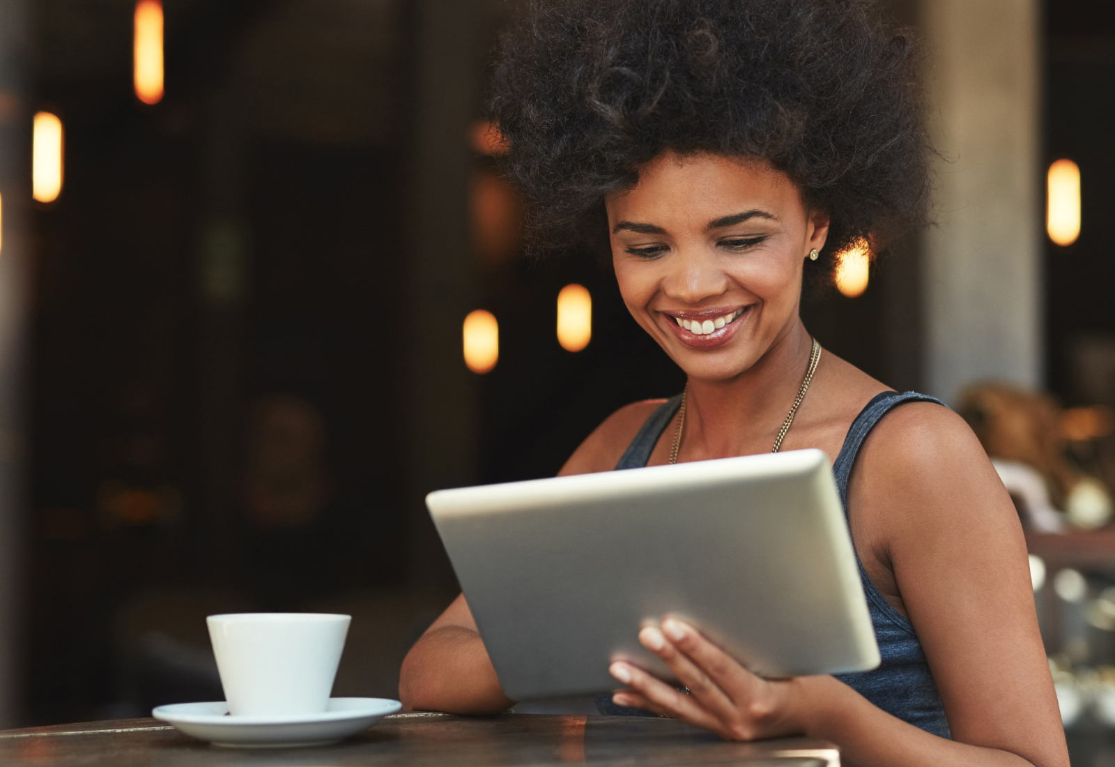 Image of a woman using a tablet and smiling while sitting at a table in a restaurant with a coffee cup