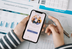 Image of a person using a smart phone with the Facebook app open on the screen over a desk full of documents and data