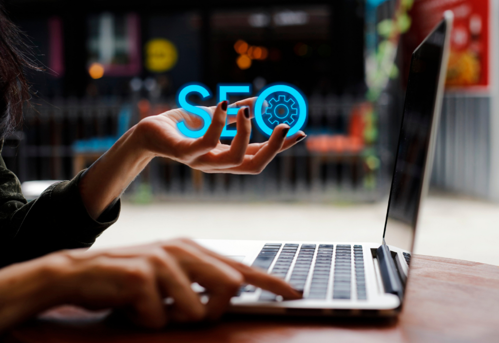 Image of a person using a laptop at a desk holding the word SEO in their hand