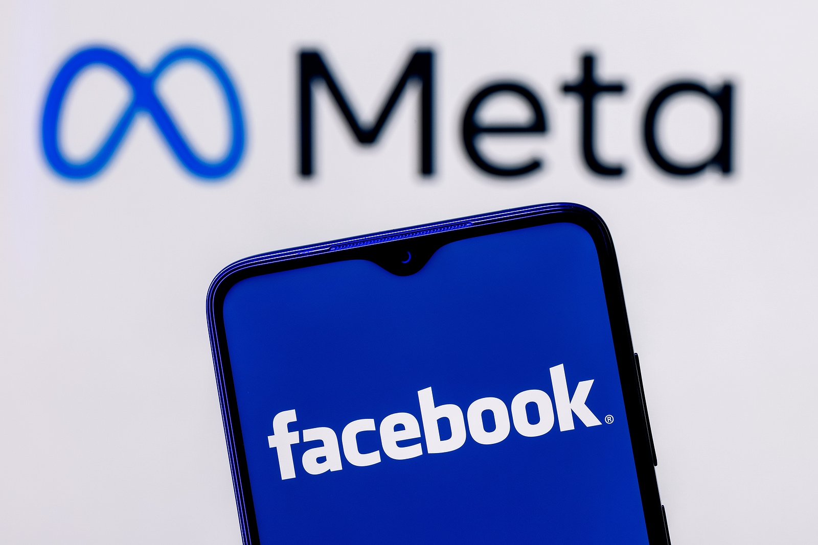 A smartphone with Facebook on the screen with the Meta logo in the background